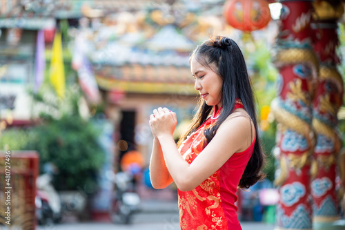 Portrait beautiful Asian girl wearing red traditional Chinese cheongsam decoration with gesture of congratulation at Chinese shrine for Chinese New Year Festival