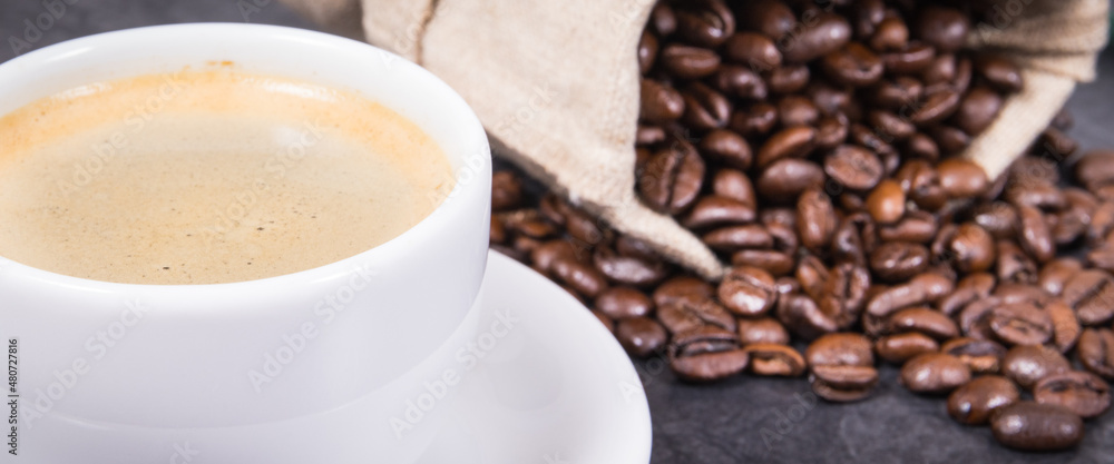 White cup of coffee and roasted fragrant dark coffee grains in bag White cup of coffee and roasted fragrant dark coffee grains in bag