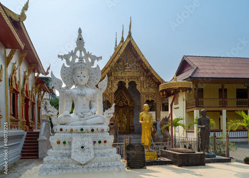 A sculpture of Buddha at the buddhist temple Wat Tung Yu in Chiang Mai  Thailand.  In the background are the Viharan  Main Hall  and Ubosot  Ordination Hall .