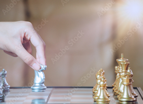 Hand businessman moving the golden knight chess fighting silver knight with fire sparks chess on chess board to successfully in the competition. Management or leadership strategy and teamwork concept.