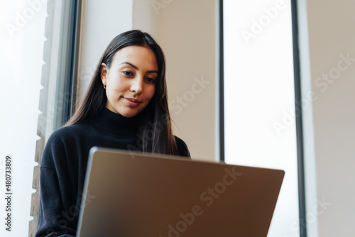 Portrait of a young woman smiling while working on laptop © contrastwerkstatt