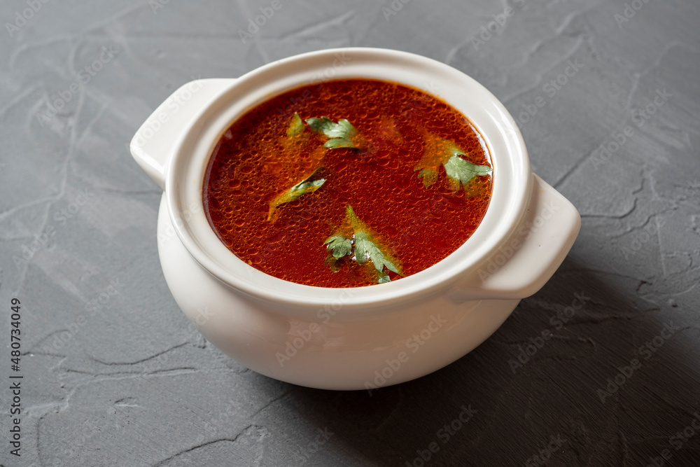 Close-up of soup borscht in a white ceramic soup bowl on a gray textured background. Traditional soup for Russia and Ukraine. Greens float on top of the soup. Side view Close-up of soup borscht in a white ceramic soup bowl on a gray textured background. Traditional soup for Russia and Ukraine. Greens float on top of the soup. Side view