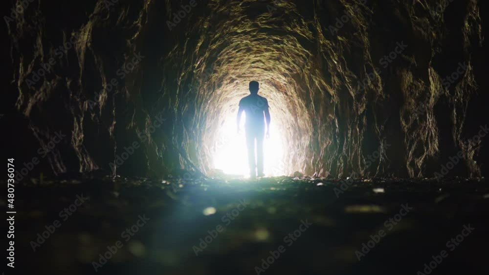 A man goes through a dark tunnel to a bright light, the concept of the exit of the soul to God's light, the mystical movement of the silhouette of a man