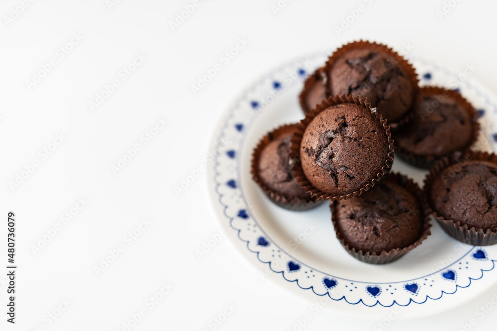 Chocolate muffins lie on a white plate with small hearts. Close-up, space for an inscription. Chocolate muffins lie on a white plate with small hearts. Close-up, space for an inscription.