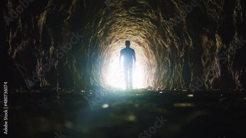 A man goes through a dark tunnel to a bright light, the concept of the exit of the soul to God's light, the mystical movement of the silhouette of a man photo