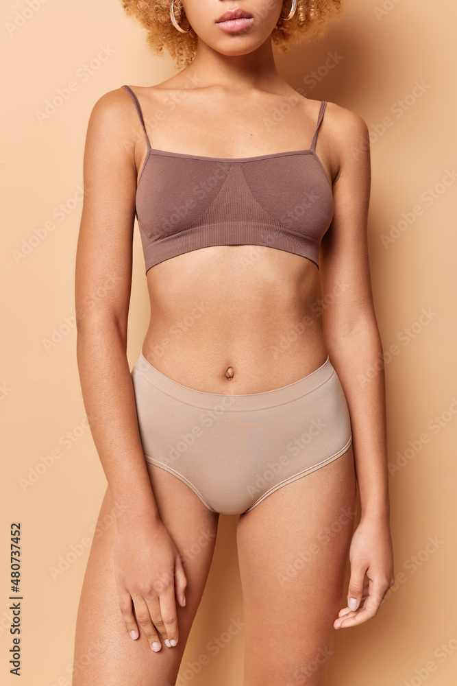 Obraz premium Wellness women body and slimming concept. Cropped shot of unrcognizable woman dressed in top and panties has flat belly healthy smooth skin and slender legs isolated over beige studio background