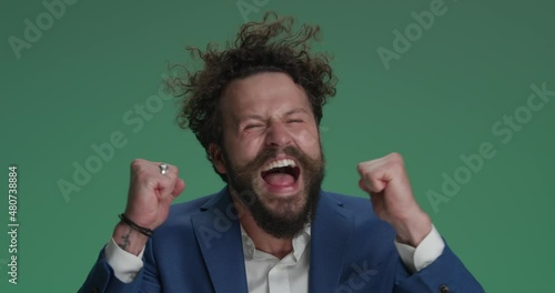 crazy businessman holding fists in the air, screaming and cheering victory, being the winner, making funny and dynamic, energy faces on green background photo