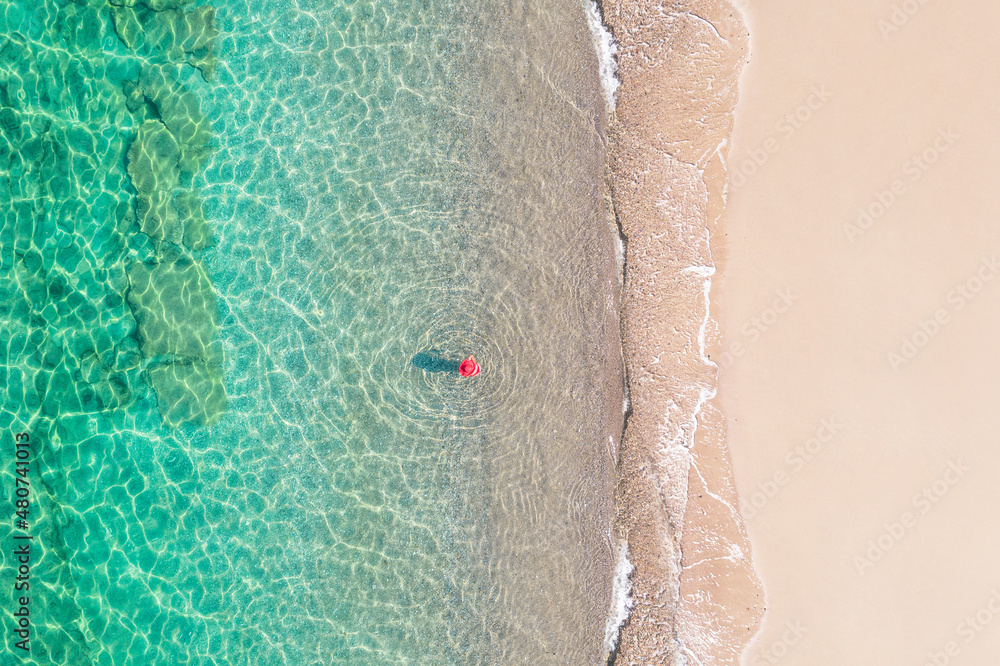 Top, aerial view. Young beautiful woman in a red hat and bikini walking, swimming, sunbathe in sea water on the sand beach. Drone, copter photo. Summer vacation. View from above.