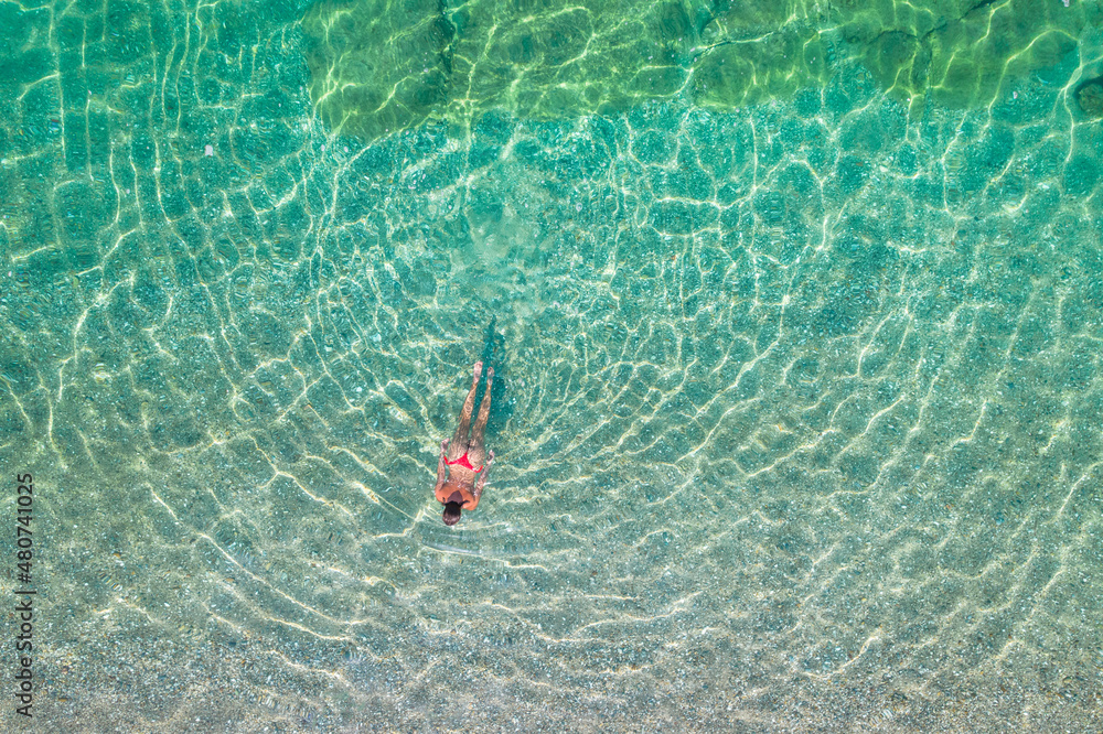 Top, aerial view. Young beautiful woman in a red bikini panties swimming in sea water on the sand beach. Drone, copter photo. Summer vacation. View from above.