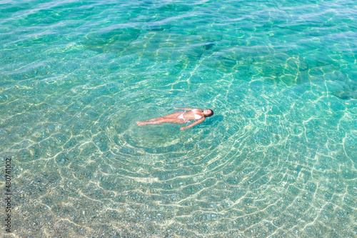 Top, aerial view. Young beautiful woman in white bikini swimming in sea water on the sand beach. Drone, copter photo. Summer vacation. View from above.