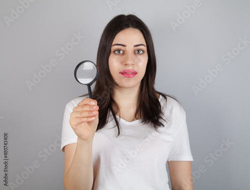  Young woman looks through a magnifying glass.