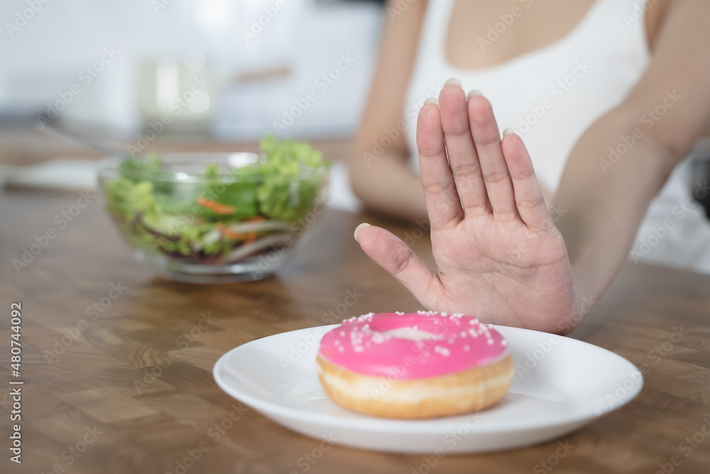 Woman on dieting for good health concept. Close up female using hand push out her favourite donut and choose salad vegetables for good health. Woman on dieting for good health concept. Close up female using hand push out her favourite donut and choose salad vegetables for good health.