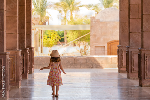 Pretty little girl walks slowly down the portico among the columns. Rear view. El Mustafa Mosque, Sharm El Sheikh, Egypt.