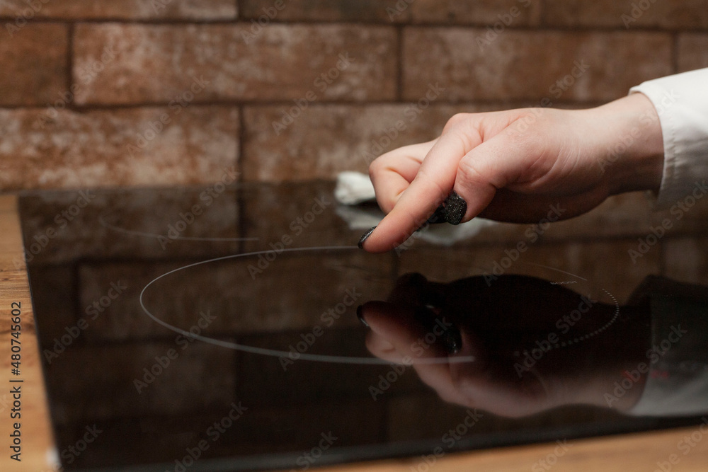 A young woman is cleaning an induction electric hob. Cleaning in the kitchen. Electric oven cleaning. Cleaning company concept. A young woman is cleaning an induction electric hob. Cleaning in the kitchen. Electric oven cleaning. Cleaning company concept.