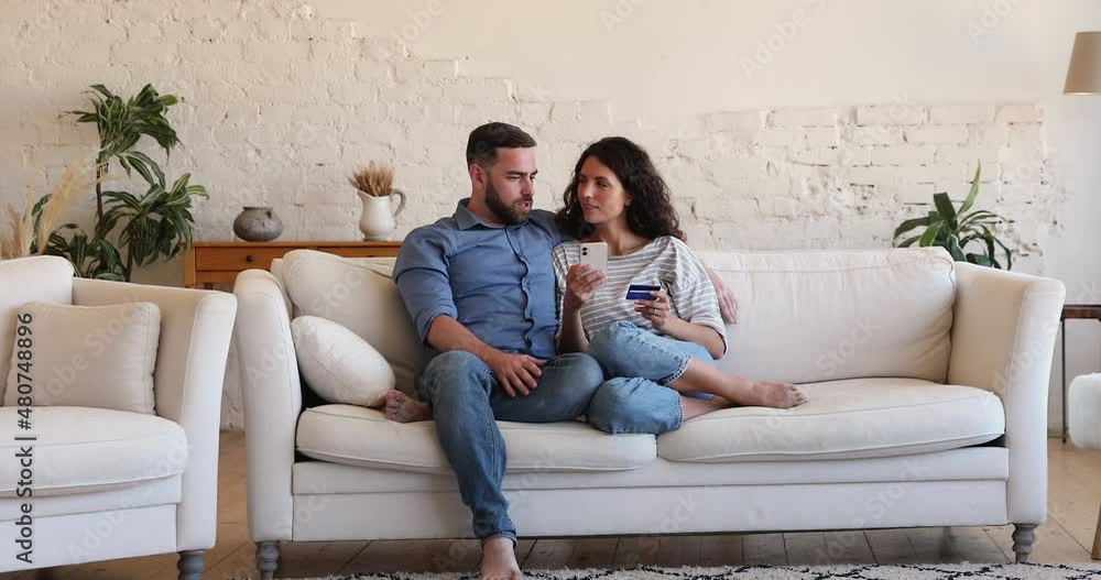 Young couple make purchase online use debit card and cellphone. Millennial spouses ordering goods, enjoy remote distancing retail services. E-commerce shoppers family spend money on internet concept Young couple make purchase online use debit card and cellphone. Millennial spouses ordering goods, enjoy remote distancing retail services. E-commerce shoppers family spend money on internet concept