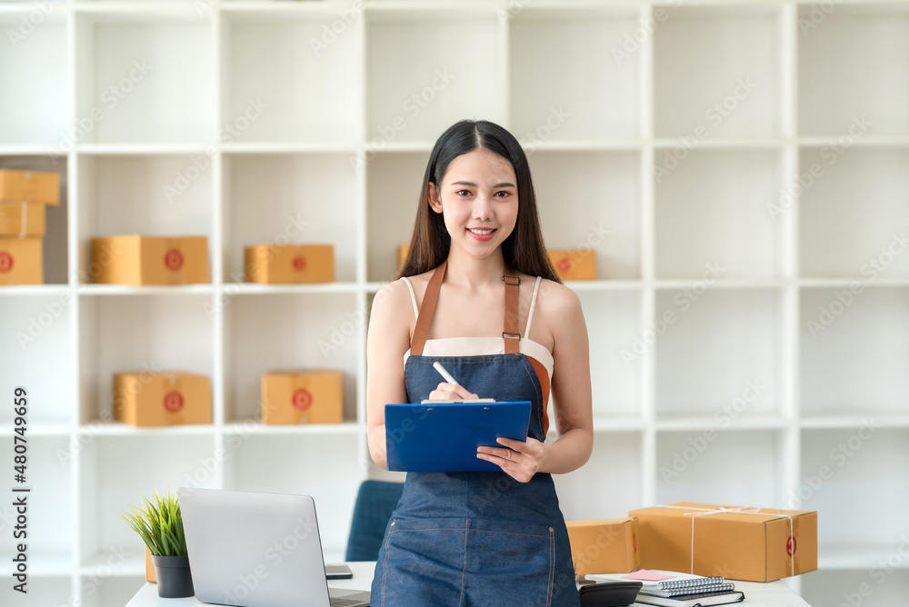 Beautiful young Asian business owner woman prepare parcel box and check online orders of product for deliver to customer. Shopping Online concept. Looking at camera. Beautiful young Asian business owner woman prepare parcel box and check online orders of product for deliver to customer. Shopping Online concept. Looking at camera.