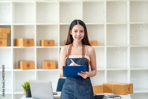 Beautiful young Asian business owner woman prepare parcel box and check online orders of product for deliver to customer. Shopping Online concept. Looking at camera.