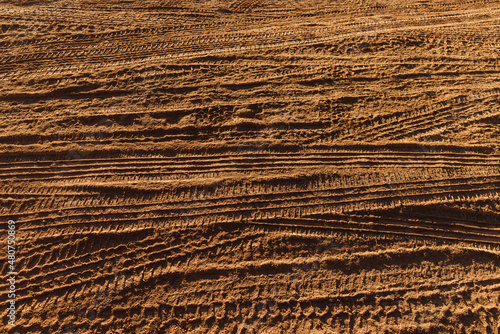 Mult layers of tire tracks print on dirty red soil in morning sunlight. Wheel marks of cars and trucks on countryside route, detail of dusty path texture background. Idea of outdoor travel and trip