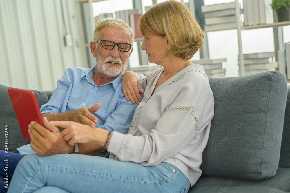Obraz premium Senior caucasian couple using tablet sitting on sofa