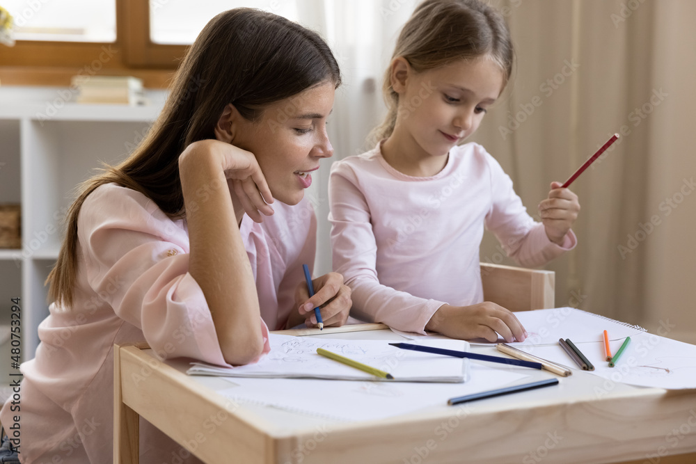 Loving 25s mom spend free time on weekend with little 6s preschool daughter holds colourful pencils enjoy painting on paper album sit together at table at home. Leisure, hobby, kid development concept Loving 25s mom spend free time on weekend with little 6s preschool daughter holds colourful pencils enjoy painting on paper album sit together at table at home. Leisure, hobby, kid development concept