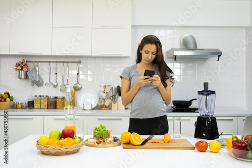 Pregnant Woman Wearing Headphone And Using Smartphone in Kitchen