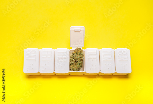 Fotografie White weekly pillbox with a big cannabis bud on yellow background with copy space