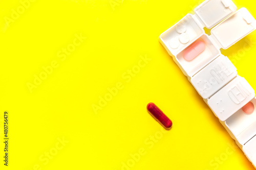 White weekly pillbox with different tablets of colors isolate on yellow background with big copy space left.