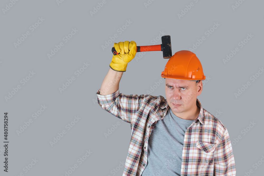 A worker in an orange hardhat hits a helmet with a hammer, protective workwear in industry A worker in an orange hardhat hits a helmet with a hammer, protective workwear in industry