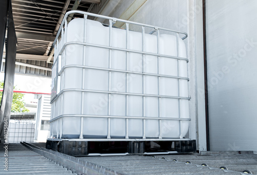 Low view with shade of a large white chemical tank on track roller inside of the factory.