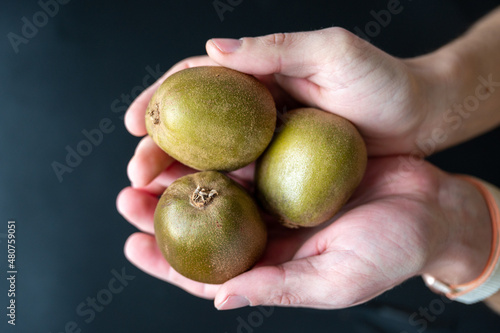 Hands holding three kiwi on dark background