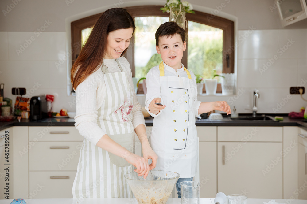 Mother with child bake muffins together in the kitchen, at home. White kitchen. Mom spends time with her son. cooking school, cooking lessons 