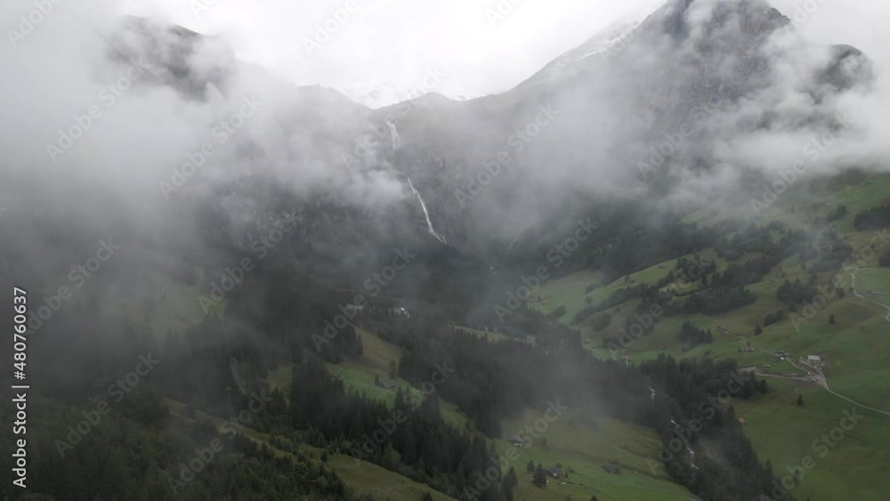 Aerial drone shot of a scenic valley in Adelboden, Switzerland. A cloudy morning of mountains with a waterfall and a small village. Low hanging clouds in the alps. Aerial drone shot of a scenic valley in Adelboden, Switzerland. A cloudy morning of mountains with a waterfall and a small village. Low hanging clouds in the alps.