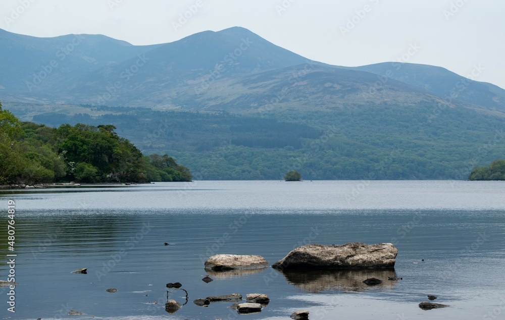 Mountains over blue glassy lake with rocks in Ireland