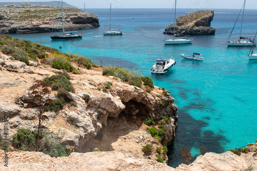 Boats floating in bright blue crystal clear water lagoon off rocky shore in Malta