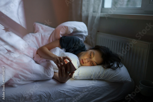 Social media jealousy. Young depressed woman addicted to mobile phone lying in bed at home, scrolling social media, feeling envious of lives of others, reading what people posting and sharing online