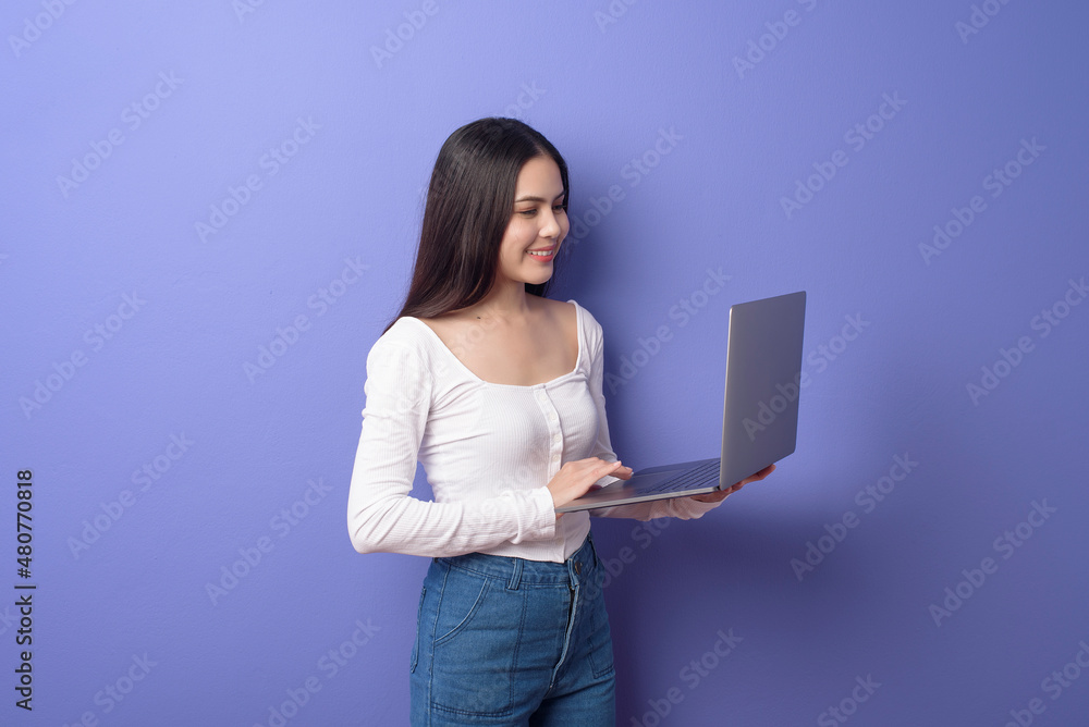 portrait of young beautiful smiling woman is holding laptop over isolated purple background studio portrait of young beautiful smiling woman is holding laptop over isolated purple background studio