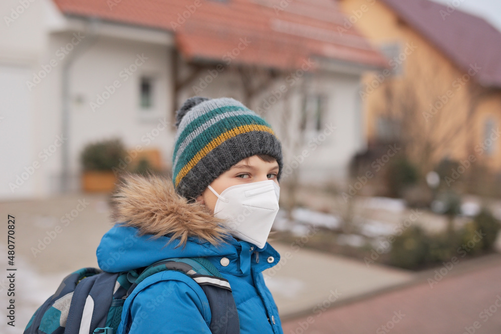 Kid boy wearing ffp medical mask on the way to school. Child backpack satchel. Schoolkid on cold autumn or winter day with warm clothes. Lockdown and quarantine time during corona pandemic disease Kid boy wearing ffp medical mask on the way to school. Child backpack satchel. Schoolkid on cold autumn or winter day with warm clothes. Lockdown and quarantine time during corona pandemic disease