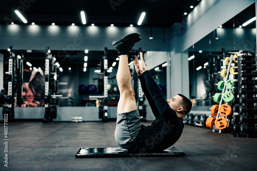 A sportsman does stretching exercises on a mat in a gym. Fotobehang
