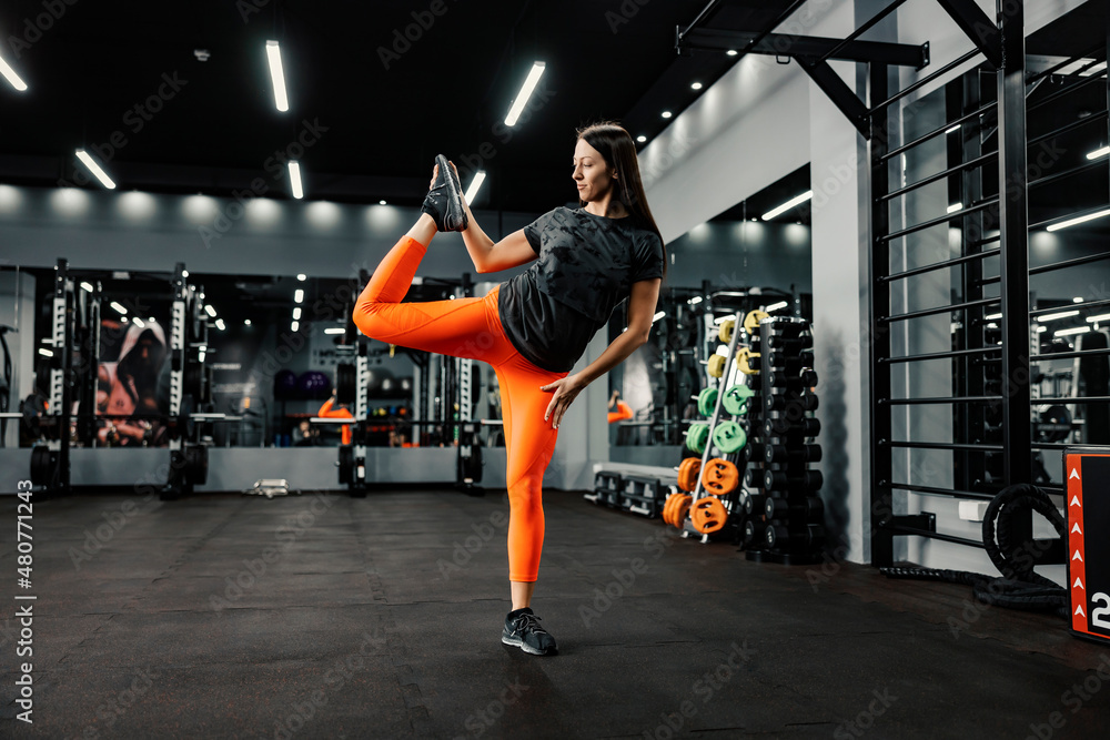 A sporty woman balance on single leg and stretching in a gym. Healthy life and fitness exercises concept.