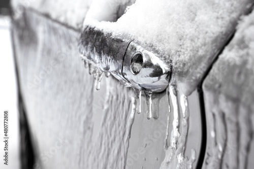 Closeup view of car door handle and lock covered in ice during winter storm. 