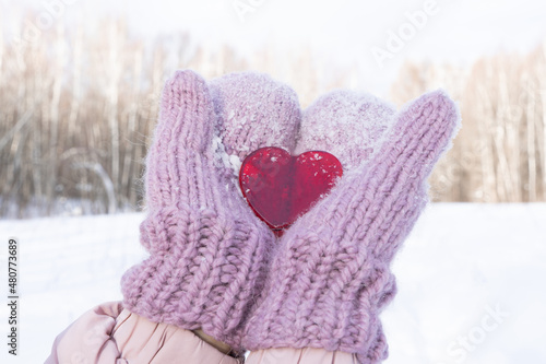The concept of the holiday is Valentine's Day. Heart in hands in warm mittens amid winter forest