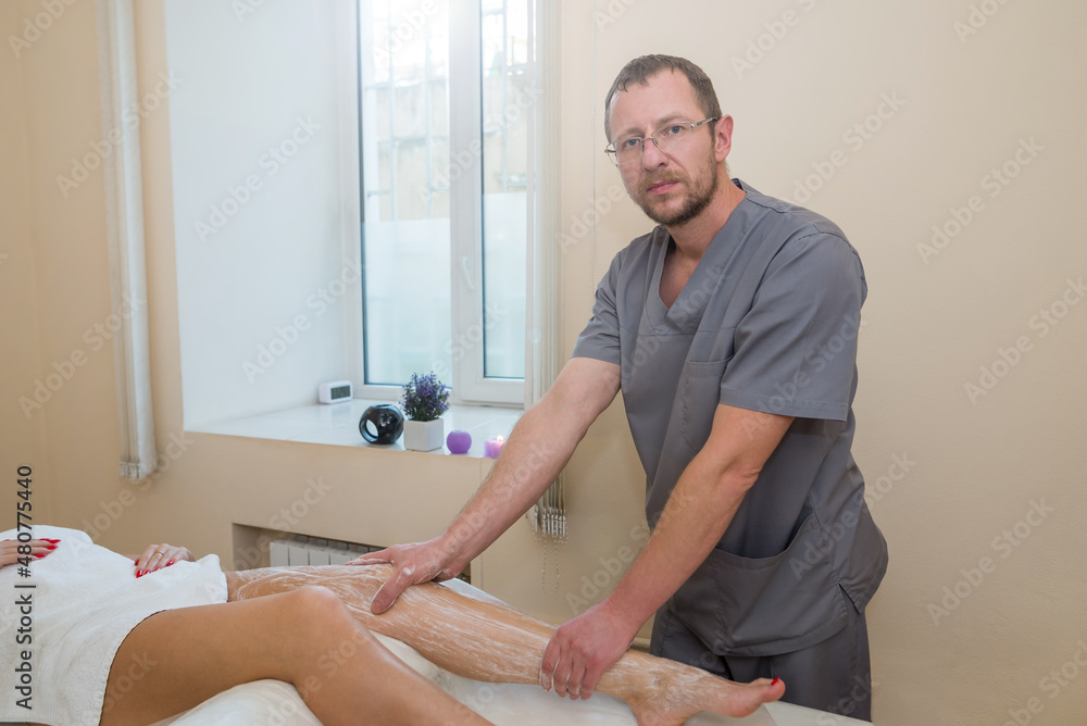 Fototapeta premium The process of scrubbing in the spa. Male massage therapist doing foot massage to young girl applying cleansing scrub