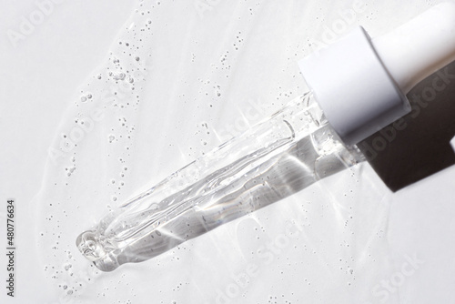 Liquid oil serum drop in pipette isolated on white background. Retinol, aha, bha acid, collagen skincare fluid, photo with shallow depth of field. Gold essence in dropper for beauty treatment photo