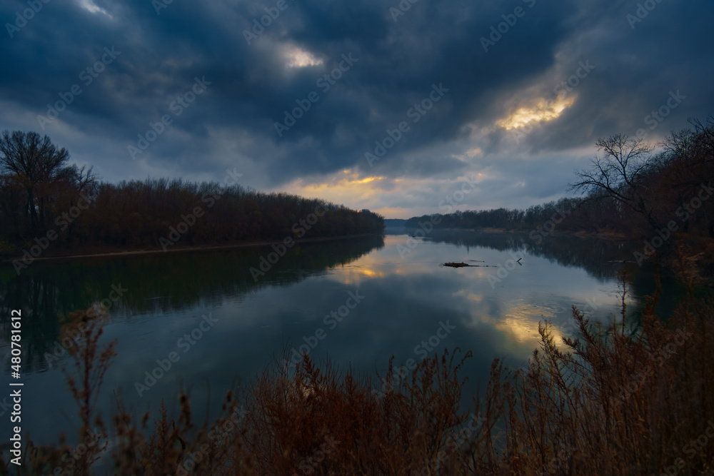 a beautiful autumn landscape in the evening - forest with river and cloudy sky