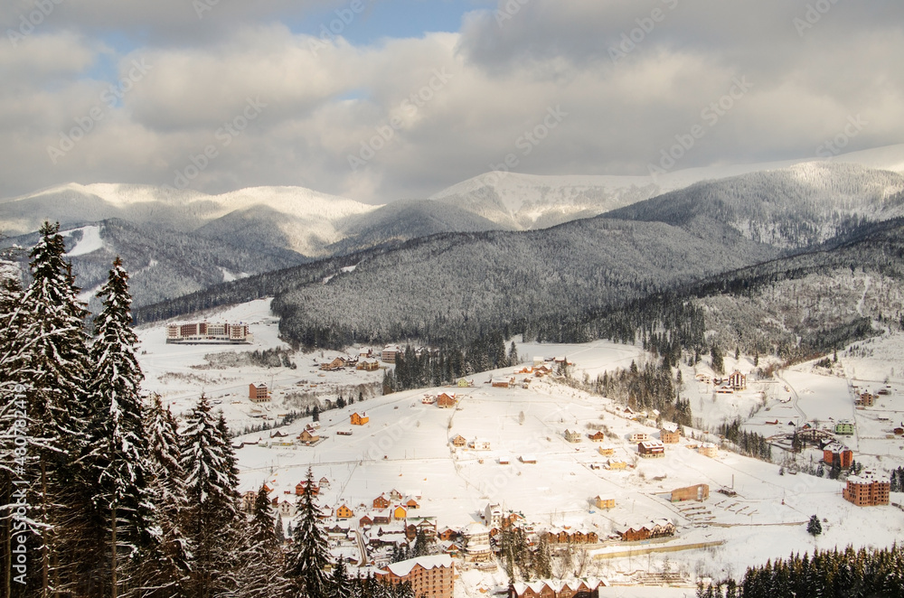 Beautiful winter landscape in the mountains. Ski resort, wooden houses and a hotel on the slopes. 