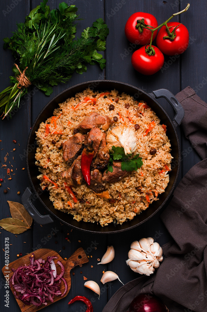 Uzbek pilaf, stewed rice with meat, in a cast-iron cauldron, on a dark gray wooden table, top view, no people, toned,