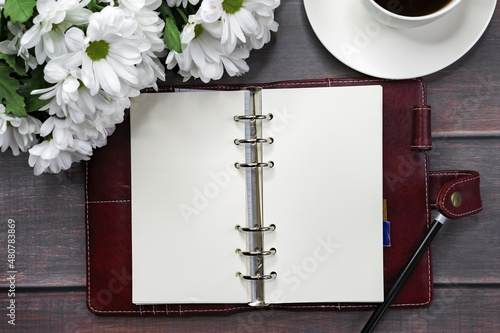 An open notebook on a wooden table with a bouquet of chrysanthemums and a cup of coffee.