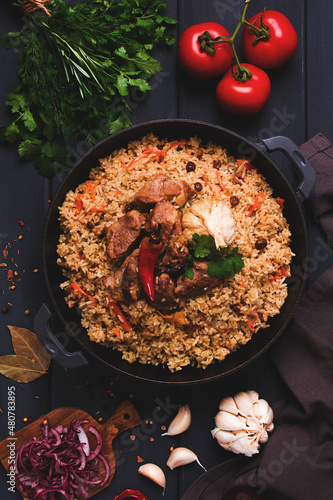 Uzbek pilaf, stewed rice with meat, in a cast-iron cauldron, on a dark gray wooden table, top view, no people, toned,