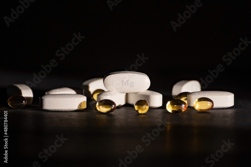 A complex of Mg ( magnesium, magnesium ) and vitamin D ( omega 3 ) capsules for the treatment and health of humans on a dark background. Copy space.