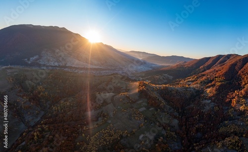 Bright sunrise at high mountains covered with autumn forest